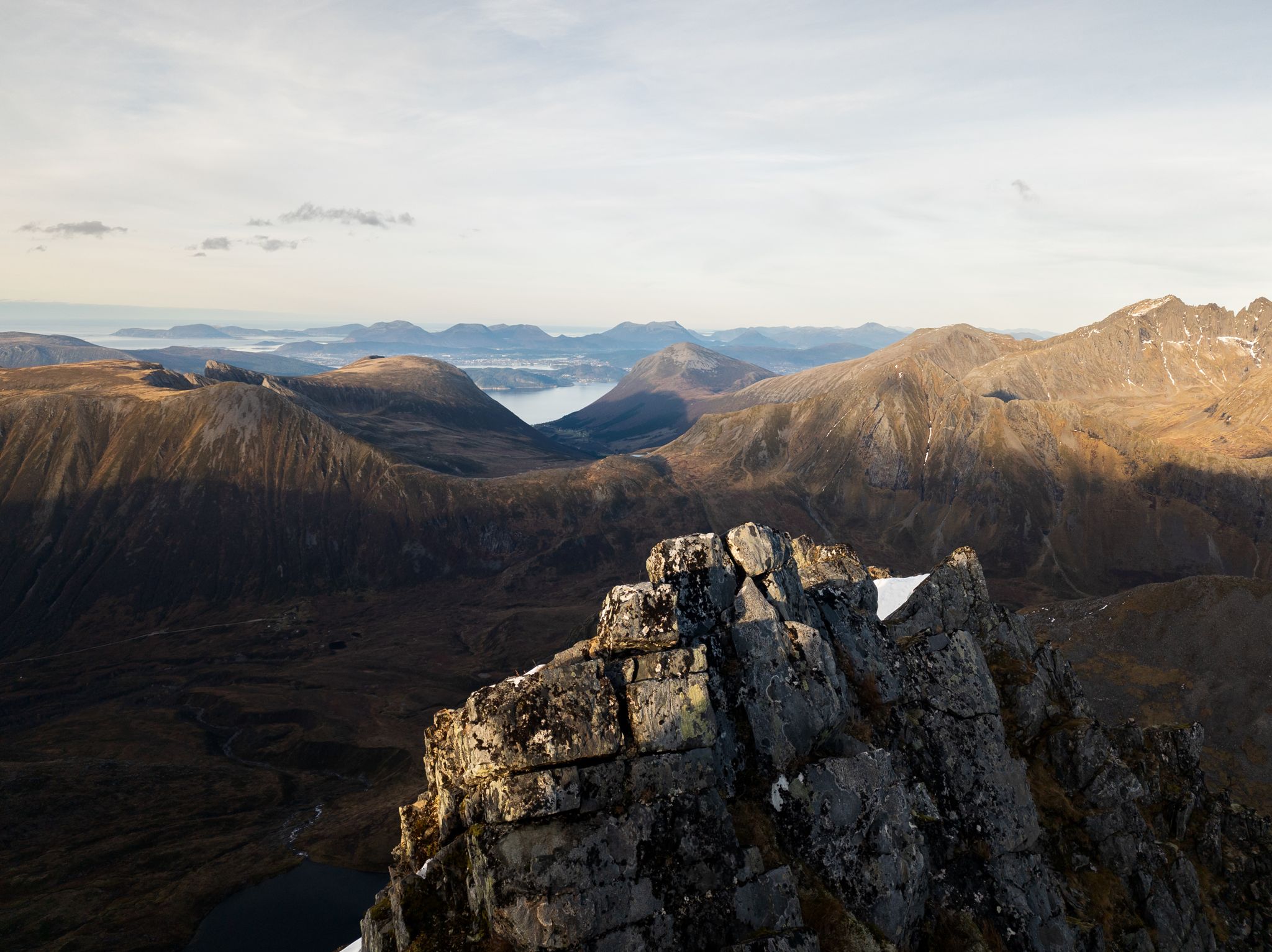 Utsikt fra en steinete rygg mot fjell, dal og fjord i kveldssol