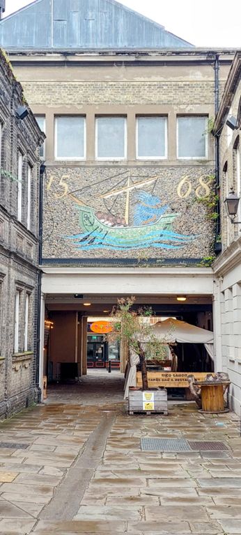 View from down the passage back to the back of the town hall.   The 1991 mosaic is of Gravesend's former 1568 coat of arms created in the year of its second charter of incorporation, which changed the market day to Wednesday and stipulated a 3 day January fair. The town's coat of arms changed in 1975.  https://www.waymarking.com/waymarks/WMH1WZ_1836_The_Old_Town_Hall_High_Street_Gravesend_Kent_UK & https://duncangrantartist.com/tag/gravesham-coat-of-arms/