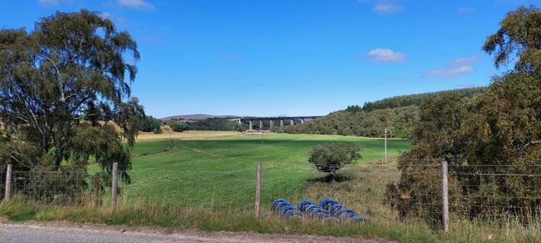Category B listed 1897 Findhorn (railway) Viaduct and the A9 bridge beyond over River Findhorn come into view after perhaps a 2 mile roll down from the summit. It had been a gentle climb up, like most climbs so far in Scotland. The next couple of photos show the plain by the River Findhorn.  About the rail bridge: https://en.wikipedia.org/wiki/Findhorn_Viaduct_(Tomatin)  About the river: https://en.wikipedia.org/wiki/River_Findhorn