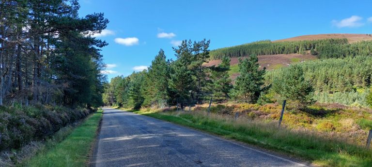 This, next and one more made into the panoramic below. After the A938 turns left into the A9, the road continues unclassified and rarely used. The dwarfing hills are the northern extent of the Cairngorms and include Carn Glas Choirr, 2162ft / 659m.