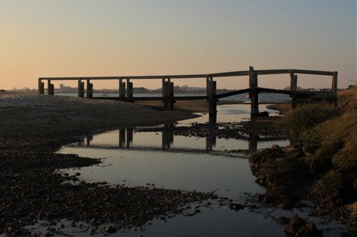 Timber bridge over a creek, with Christchurch Priory just about discernable in the background
