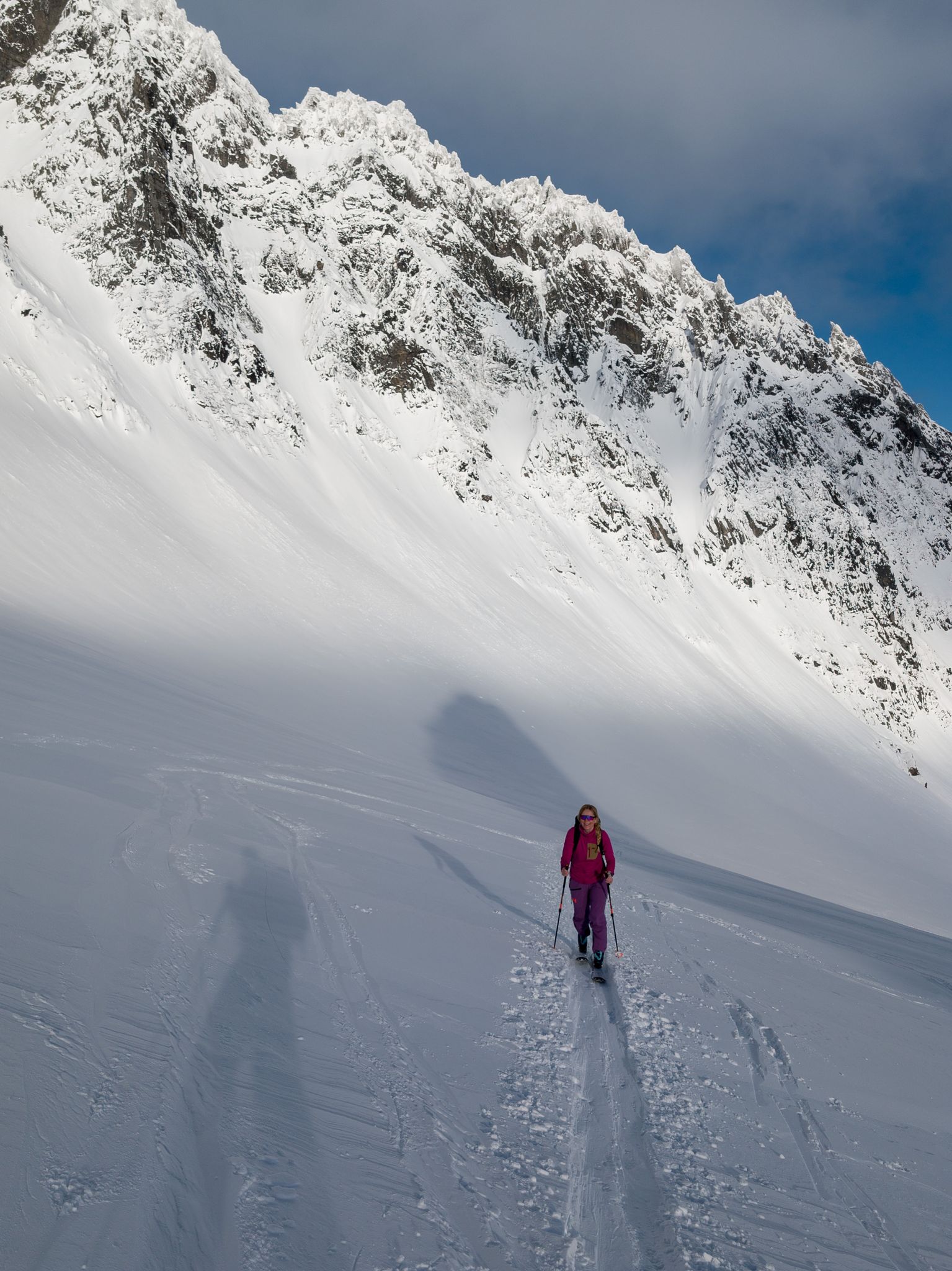 Skiløper i snøflanken under en bratt og taggete fjellvegg
