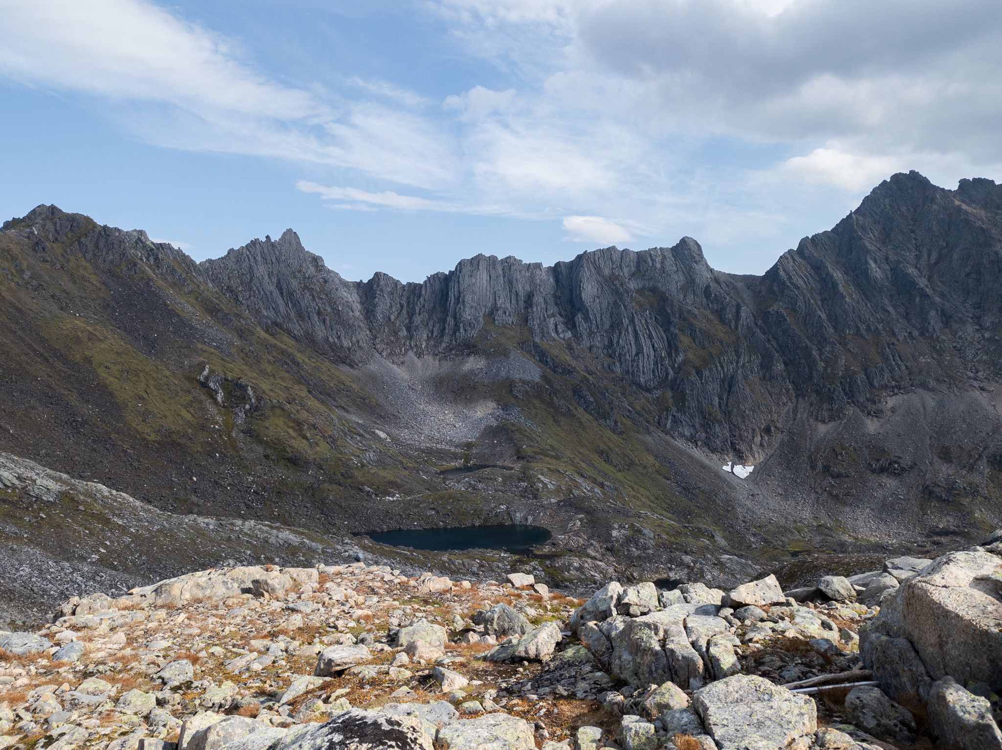 Taggete fjellrygger og et lite mørkt fjellvann ved Storegjøltinden