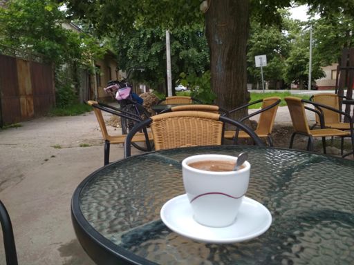 Чашечка кофе в единственном кафе. Остальные столики пусты. Детское сиденье на велосипеде перекинуто вперёд, чтоб не мешало крутить педали