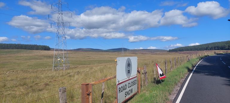 4.7 miles out of Alness, I took this photo for the "Road closed snow" gate on the B9176 Struie Road, and the smoothness of the road.  If that is possible this far north, then it is possible on the A74 and NCN Route 74 in South Lanarkshire on Day 25.  The horizon consists of l>r  the forested edge of 2270ft/692m Beinn Tharsuinn, Beinn Tharsuinn Wind Farm 1673-1791ft /  510-546m high, 1749ft/533m Meall Meadhonach, 1729ft/527m Meall a' Bhreacain with the forested 1214ft/370m Meallan Dubn hill on the right.  Beinn = Scottish Gaelic for hill, mountain, pinnacle. https://www.wordsense.eu/beinn/#Scottish_Gaelic