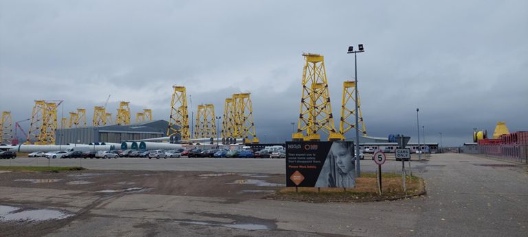 Global Energy Group's Nigg Energy Park at the Port of Nigg.  http://nigg.com/  Research since reveals the grey items are wind turbine parts for the wind farm near Ben Klibreck south of Altnaharra, and the yellow uprights are some of the 114 "jacket foundations" for the Seagreen fixed bottom offshore wind farm estimated to generate power for 1.6m homes.  ABOUT NIGG: https://en.m.wikipedia.org/wiki/Nigg,_Highland & ABOUT GREY WIND TURBINE PARTS: https://energydigital.com/renewable-energy/wind-turbine-deliveries-underway-at-Creag-Riabhach-Wind-Farm & ABOUT YELLOW JACKET FOUNDATIONS: https://www.sserenewables.com/news-and-views/2022/09/seagreen-wind-farm-celebrates-jacket-installation-milestone/