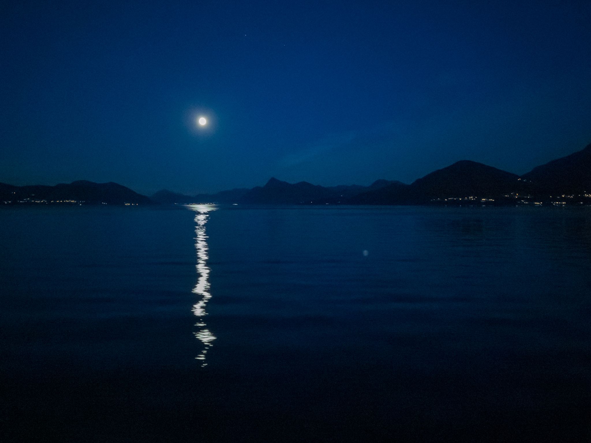 Lys måne over fjorden med speiling i vannet og fjell i silhuett