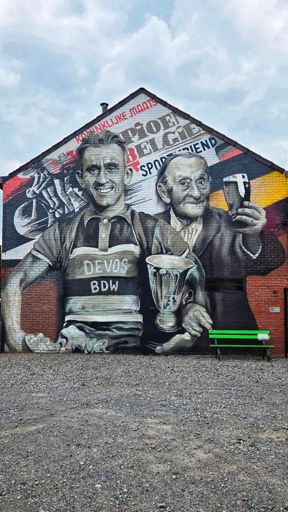 Ter hoogte van Heirweg 108 te Sint-Baafs-Vijve (het kruispunt van de Heirweg met de Abeelestraat) is een muurschildering aangebracht ter ere van oud-wielrenner en cafébaas Boudewijn Devos. Het kunstwerk - ontworpen en uitgevoerd door Treepack BV - werd aangebracht aan de gevel van het huis van zijn zoon Patrick.

Op 16 juni 2022 werd de muurschildering officieel ingehuldigd in aanwezigheid van o.a. familie van Boudewijn Devos, oud-wielrenner Lucien Van Impe en ereburgemeester Noël Demeulenaere. 

Boudewijn Devos (°30/09/1929) was een getalenteerd jeugdrenner: hij behaalde als amateur-renner vele overwinningen. Als prof nam hij deel aan diverse koersen zoals De Ronde van Marokko en De Omloop van de Grensstreek Moeskroen; deze laatste won hij ook. Nadat hij in 1957 zijn fiets aan de haak hing, begon hij een café en fietsenzaak op de Heirweg. Café De Sportvriend werd een begrip in de wijde omgeving – net als Boudewijn Devos zelf: hij was gekend en geliefd door iedereen in Wielsbeke.

In het kunstwerk “Boudewijn & Devos” staat de jonge wielerkampioen Boudewijn arm in arm met zijn oudere zelf: Boudewijn als gezellige cafébaas. Centraal in het ontwerp staat zijn lach, die tweemaal boekdelen spreekt, en die passanten nog vele jaren zal verwelkomen in Wielsbeke.

Café De Sportvriend werd eind 2020 – 3 jaar na het overlijden van Devos – afgebroken om het kruispunt van de Heirweg met de Abeelestraat verkeersveiliger te maken. Op de plaats van het voormalige café is Devos nu vereeuwigd.

