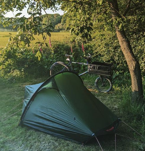 A tent pitched amongst some trees with a cargo bike in the background.